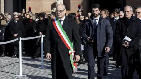 EPA/Shutterstock Rome’s mayor, wearing a tricolour sash, walks among mourners outside the basilica after the funeral.