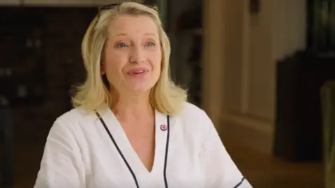 Reform UK Blonde-haired Sian Astley, wearing a white top, speaks to the camera in a Reform visor