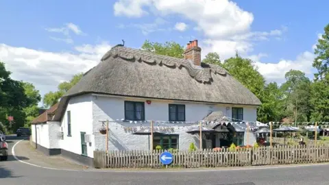A thatched-roof pub on the corner of a bend in the road.