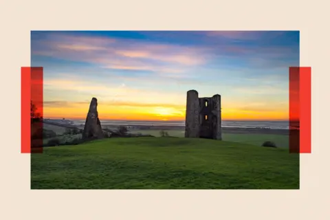 Universal Images Group The ruins of Hadleigh Castle silhouetted against an orange winter sunset and green hills