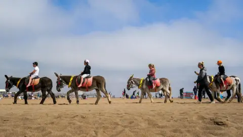 Getty Images a sunny day on skegness beach, with a row of youngsters riding on donkeys 