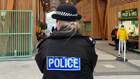 Andrew Turner/BBC A female police officer wearing a police uniform and hat is standing inside Great Yarmouth's market building. She has her back turned to the camera.