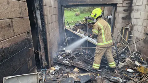 Bentham Fire Station A firefighter sprays water towards the floor in a burnt-out house.