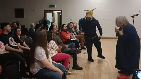 Mark Nicholas A man with a slug hat speaks to the a crowd with a lady behind him performing sign language.