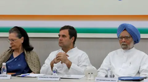 Reuters Rahul Gandhi, President of Congress party(c) wearing a white traditional indian shirt sits with his hands folded, his mother and leader of the party Sonia Gandhi is wearing a navy blue saree with an olive green scarf a and India's former Prime Minister Manmohan Singh wearing a white traditional indian shirt and hus trademark blue turban attend a Congress Working Committee (CWC) meeting in New Delhi, India, May 25, 2019.