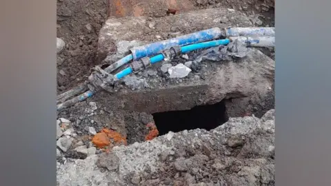 Grey concrete Victorian sewer, with blue water pipes on top of it.