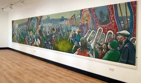 Durham County Council A large colourful mural showing crowds of people and musicians carrying banners at the gala.