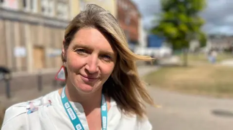 Nicola Hughes, is wearing a white top with buttons and an InExeter lanyard.