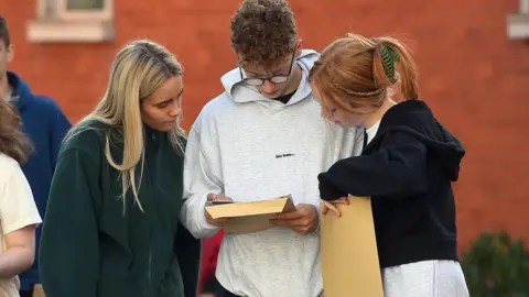 PA Three young people are looking at a piece of paper with exam results and holding envelopes