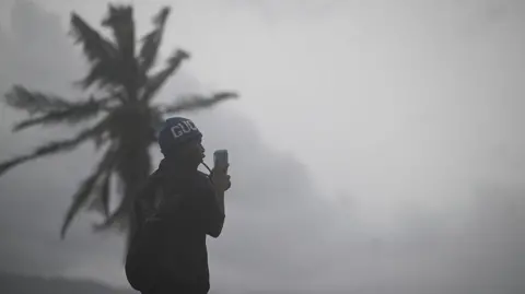 Getty Images A man uses his cellphone at the waterfront in Kingston on October 27, 2025