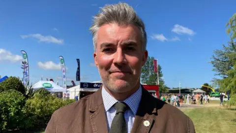 BBC/Cara Thorpe A shot of York and North Yorkshire Mayor David Skaith at the Great Yorkshire Show. He has short, grey hair and grey stubble and wears a brown jacket, purple checked shirt and dark green tie.