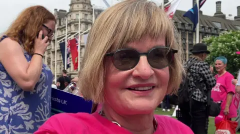Pamela has a short, dark blonde bob and wears a flamingo pink Dignity in Dying campaign tee-shirt