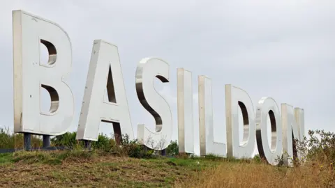A giant white statue on a grassy bank spells out BASILDON in giant letters. It is cloudy above.