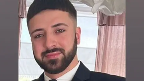 Hertfordshire Police Kyle Clifford dressed in a dark suit and tie, with a beard and brown eyes 