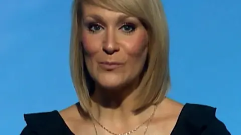 Woman in black top with hands linked in front of her in front of a blue background.