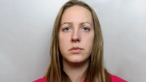 A custody photograph of Lucy Letby who has long blonde hair and and is wearing a red top.