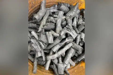 Peter Barker / National Trust An aerial view of a rusty metal container brimming with dozens of grey pieces of wood, that appear to have been burnt.
