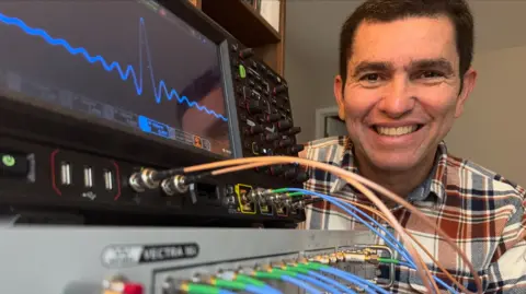 Fabio with some electronic devices showing the smiling face of Da Silva and showing a screen a wave readout.