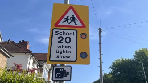 Sign that reads "School, 20 when lights show" and a speed camera signal. 