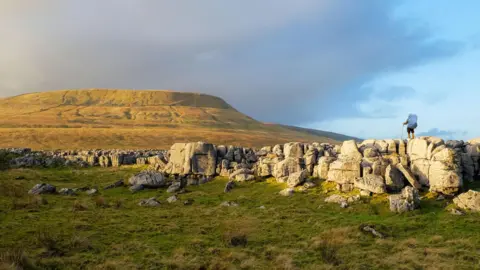 A backpacker walks along rocks at the bottom of Ingleborough