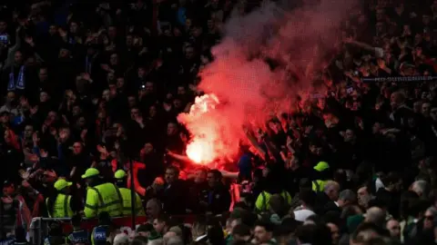 Sns a red torch that is drained in the middle of a lot of football fans