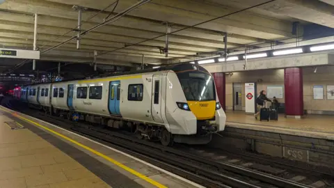 Getty Images Front view of a Thameslink train stopped at Farringdon Station with a passenger running with two pieces of luggage on the platform after getting off the train in early morning