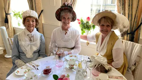 Three women sat at a table wearing period costumes.