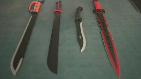 Four zombie knives on a table, with red and black handles and similar blades