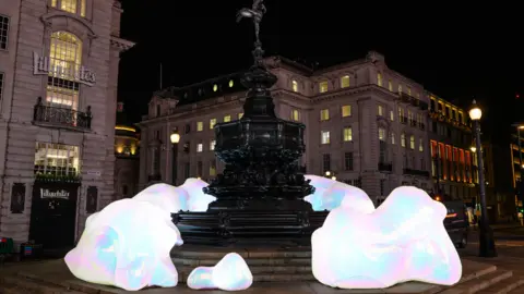 Art of London/PA Media Sculptures of asteroid-shaped iridescent boulders are pictured in front of Lillywhites with other buildings in the background