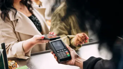 A woman tapping her phone on a card reader to make a contactless payment