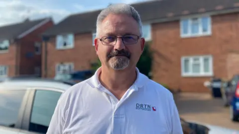 An image of driving instructor Paul Whitburn standing in front of his car