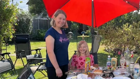 Olha and Mira eating in a garden under a parasol