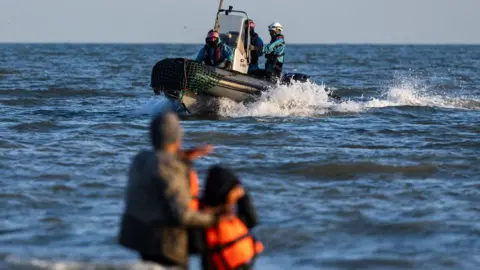 A French Navy boat sails past migrants trying to board a boat in an attempt to cross the English Channel 