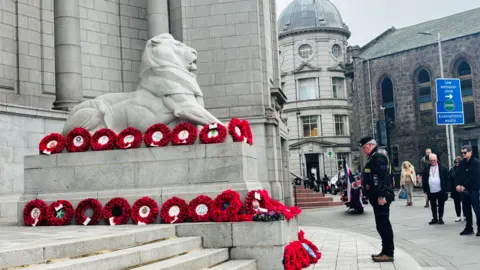 Aberdeen silence was held at Cowdray Hall as a man stands paying tribute to a display of wreaths made of poppy's organised on a lion statue.