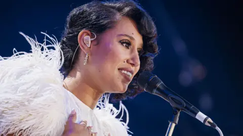 EPA Raye on stage in front of a microphone and wearing a feathered white outfit at the Montreux Jazz Festival in July 2024