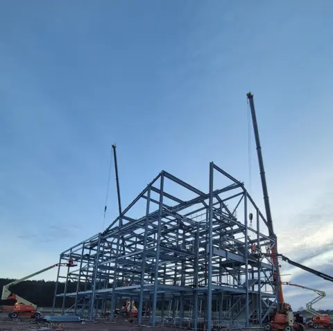 Highland Council The steel frame of the new school buildings being erected. There are several cranes on the site.