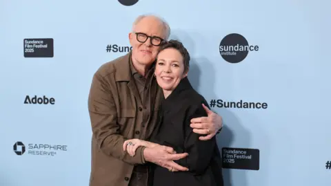 Neilson Barnard / Getty Images John Lithgow iswaring a brown shirt and top and hugging Olivia Colman who is in a black jacket. They attend the "Jimpa" Premiere during the 2025 Sundance Film Festival at Eccles Center Theatre on January 23, 2025 in Park City, Utah. 