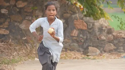 Sushila Meena, 10, wearing her school uniform - a pale blue tunic and faded navy blue pants - holds a ball in her hand as she performs her viral bowling action