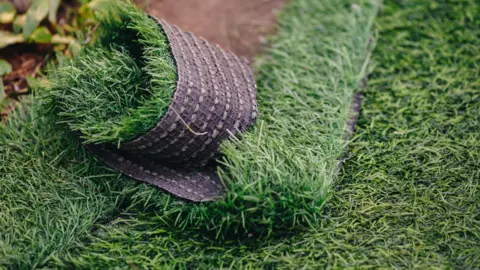 A stock image of fake grass, with some laid out and another part twisted in a ball.