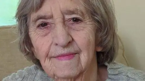 Emma Finch faces the camera, half-smiling. She has neck-length light-brown/grey hair and wears a light grey jumper.