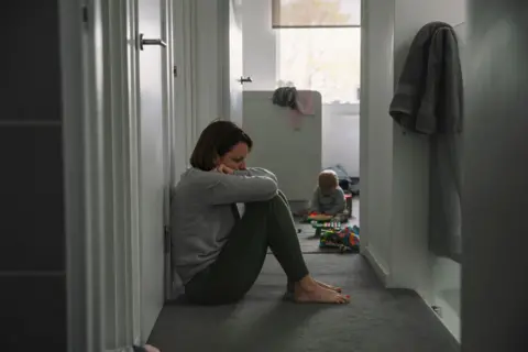 Generic picture of a mother sitting on the floor with her baby in the background