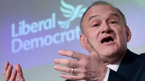 Sir Ed Davey giving a speech in front of a backdrop reading Liberal Democrats.