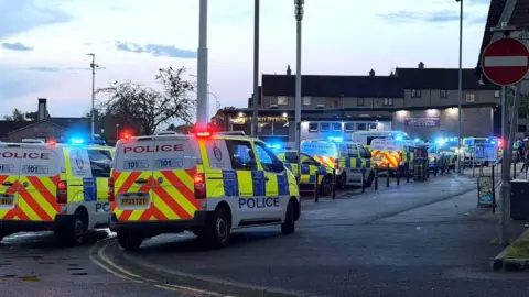 Multiple police vehicles under blue lights at the scene of what was described as a youth disorder incident.