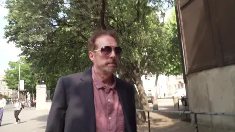 Chris Brain leaves Inner London Crown Court, wearing a purple shirt under a blue suit jacket.