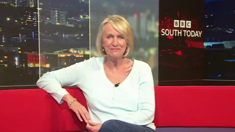 Sally Taylor sits on a red couch with a South Today banner in the TV studio