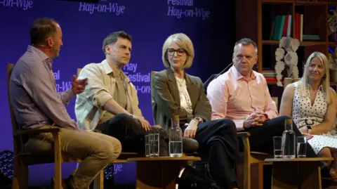 BBC Wales Broadcaster and former Downing Street director of communications Guto Harri talks to political journalist and author, Will Hayward, BBC Cymru Wales journalist and presenter, Bethan Rhys Roberts, Welsh MP, Nick Thomas-Symonds, and Plaid Cymru MS, Sera Evans. They're all sat on the stage looking at Guto Harri. 