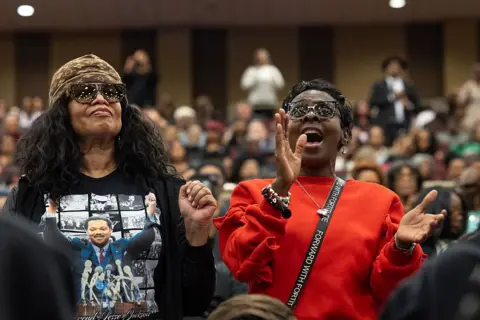 Getty Images Two women are seen standing and singing at the funeral service.