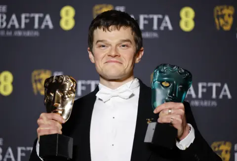 Actor Robert Aramayo holding two Baftas