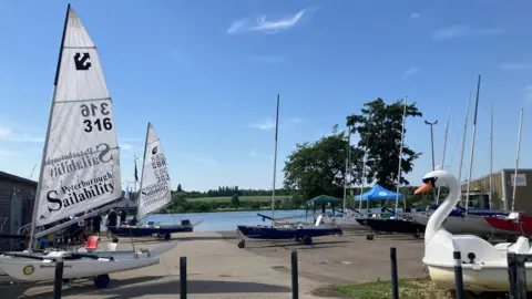 Shariqua Ahmed/BBC White sailing boats and swan boats parked near the water.