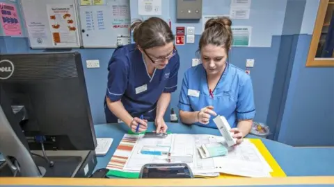 Science Photo Library Nurses talking at a desk